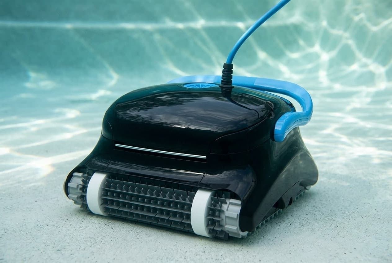 A glossy black Dolphin Nautilus CC Plus robotic cleaner on the floor of a pool, a silver strip across its front above gray spiked brush rollers, a blue vent on top, a bright blue handle laid back over the rear, and a blue cable rising from the top