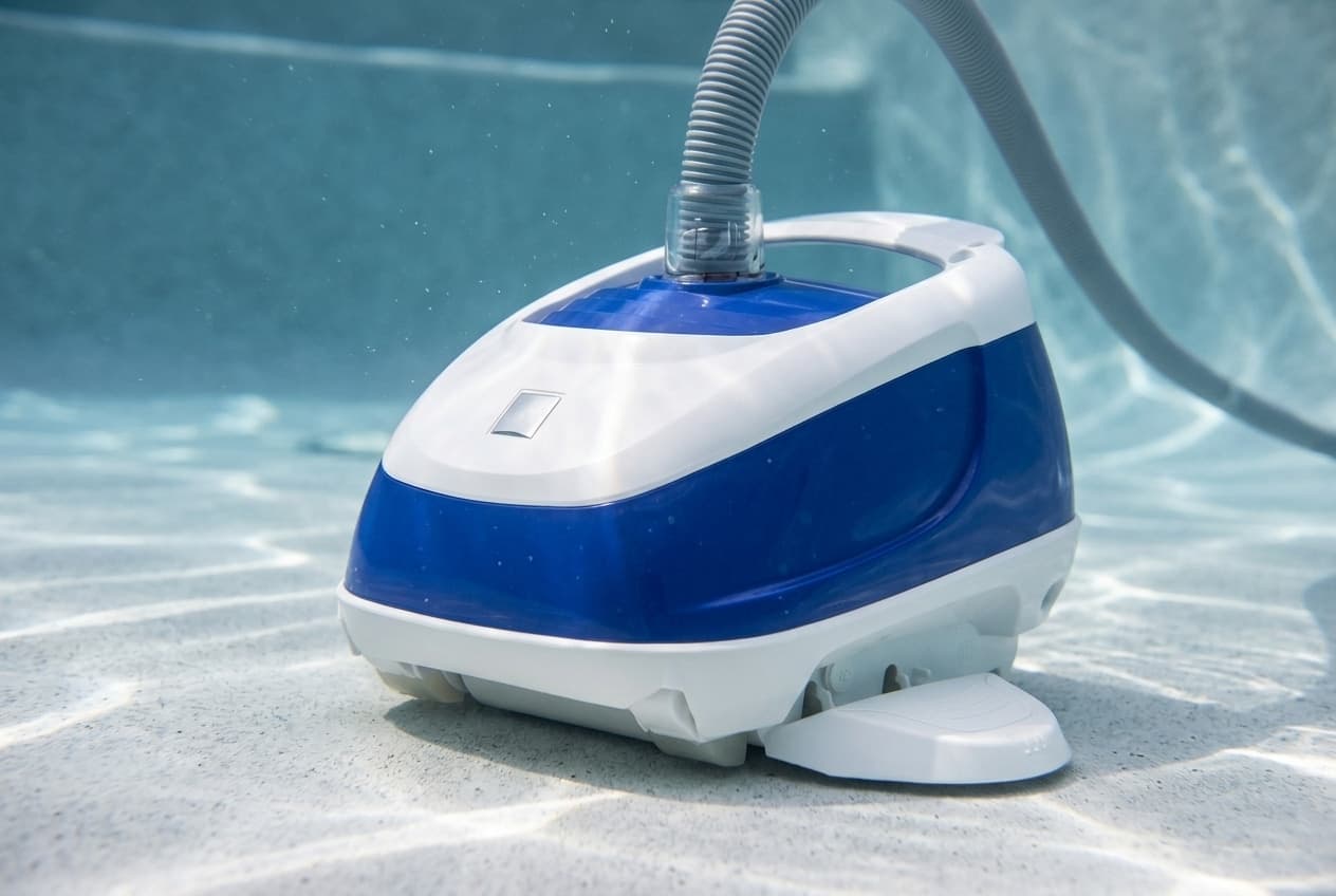 A blue and white Hayward Navigator Pro suction cleaner on the plaster floor of a pool, its gray hose curving up from the clear swivel on top