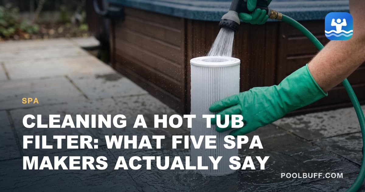 Hands in green rubber gloves rinsing a white pleated hot tub filter cartridge with a hose nozzle, the cartridge standing on wet stone pavers beside a hot tub cabinet